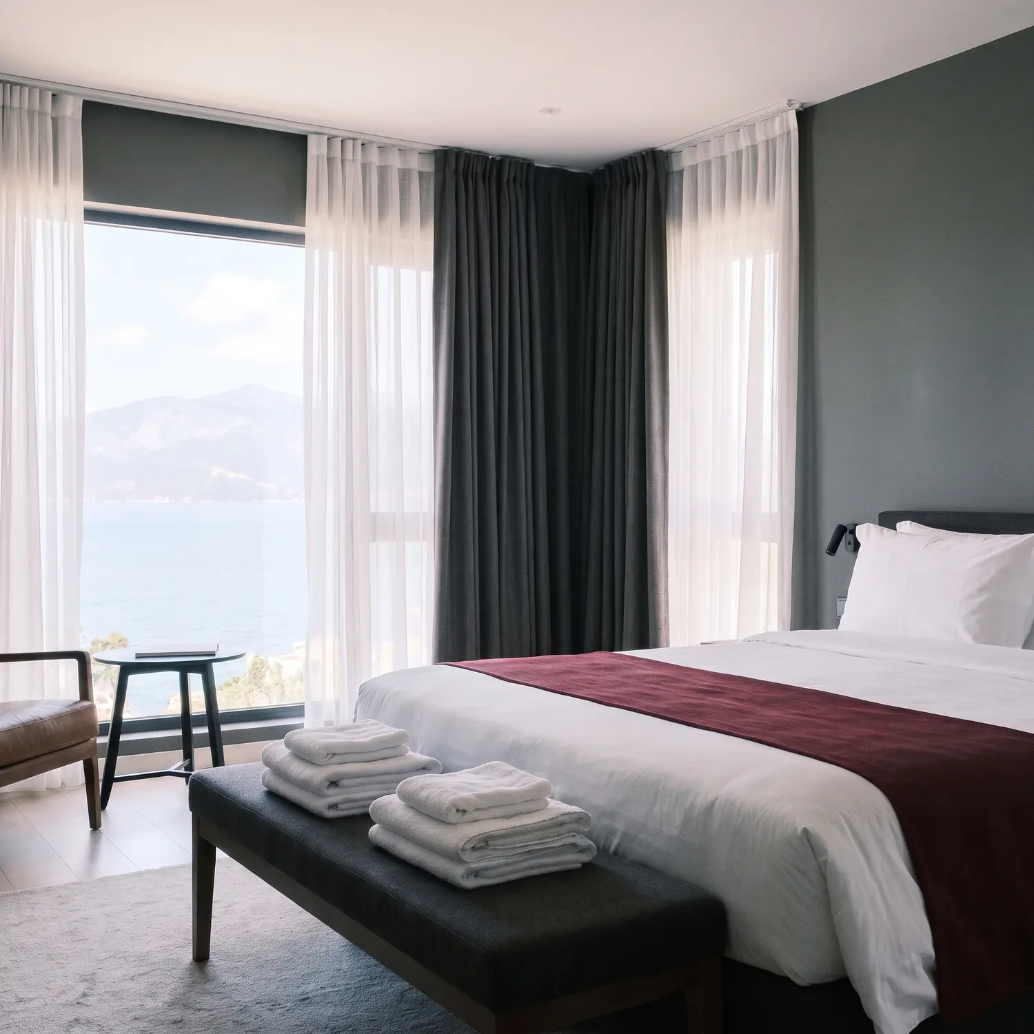Guest-ready hotel room with white bed linen, a burgundy bed runner and folded towels by Linen and Co